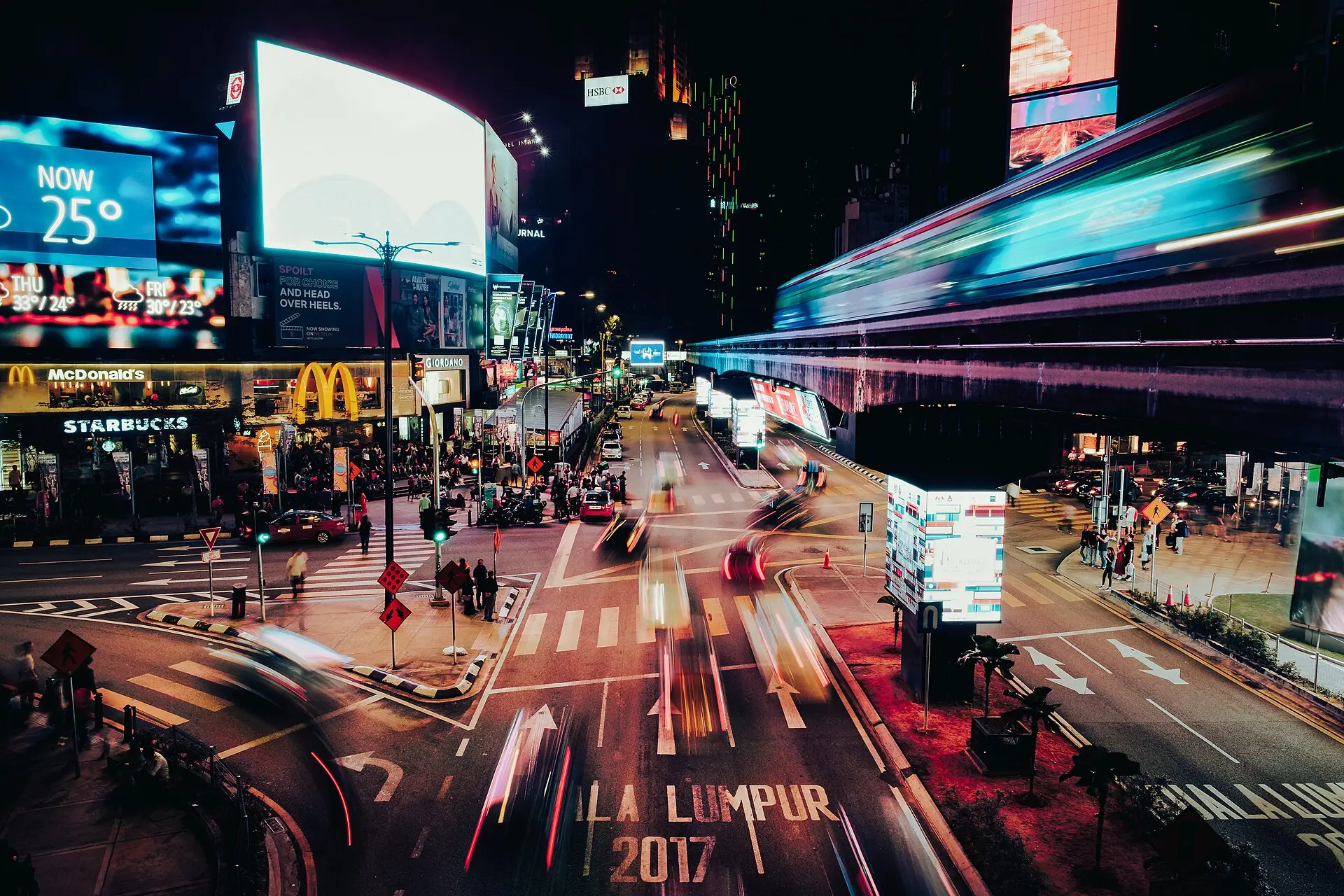 Neon signage and traffic light trails on a Kuala Lumpur street at night