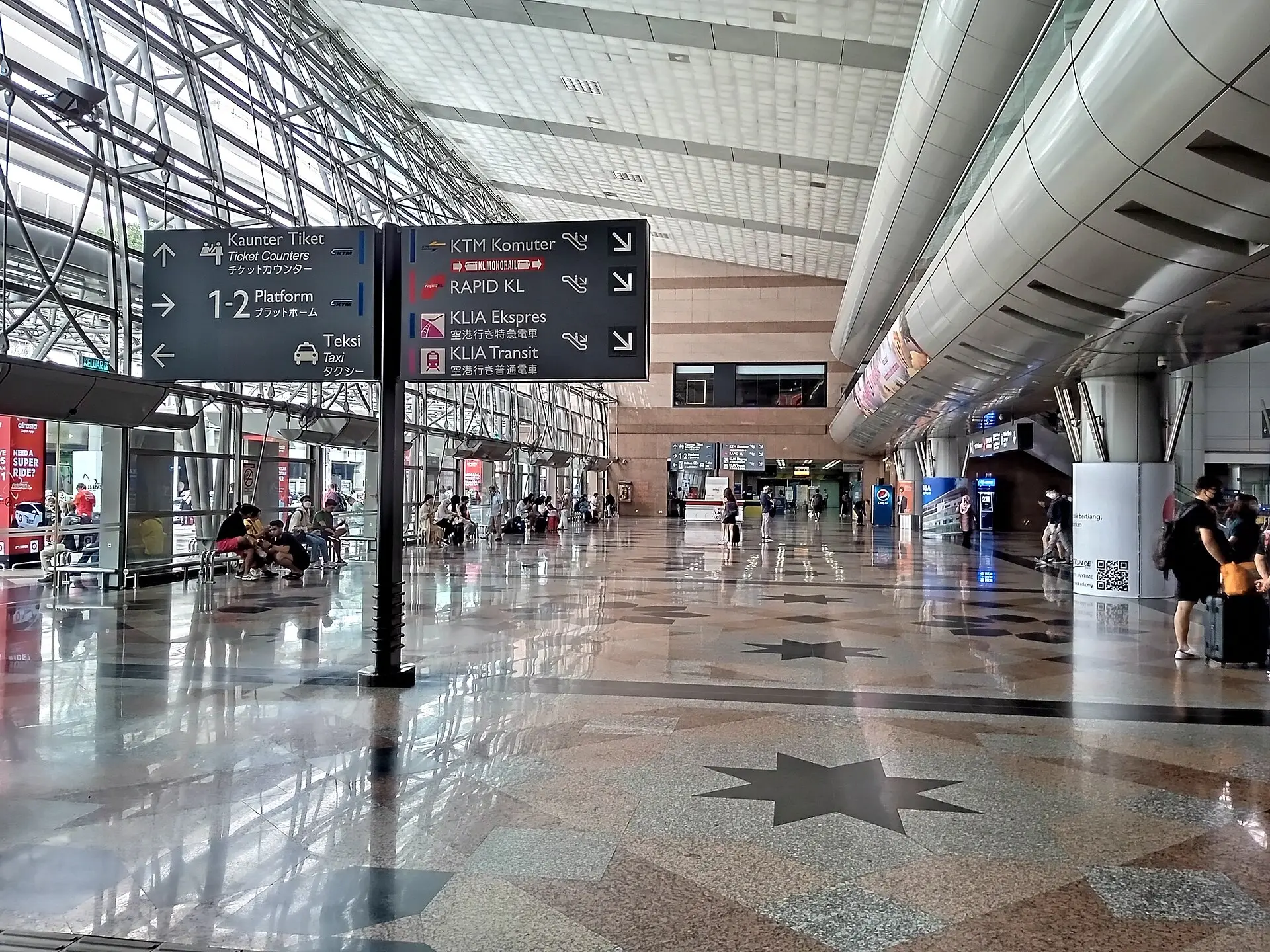 Commuters crossing the main concourse at KL Sentral station beneath overhead signs for the MRT and KTM lines