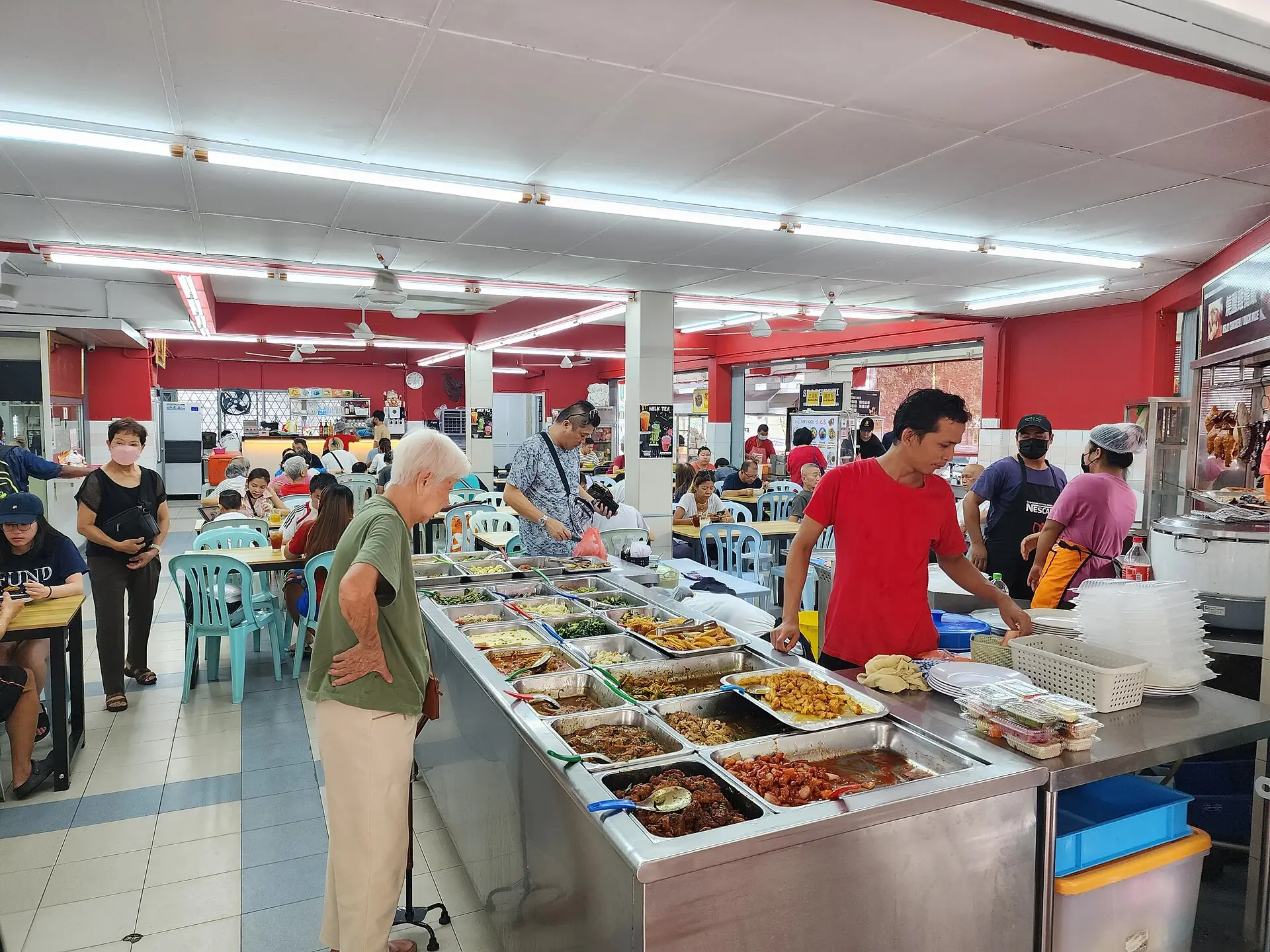 A busy Malaysian kopitiam with a counter of curries and stir-fries and customers eating at simple tables